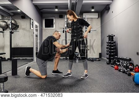 The Concept Of Modern Training. A Male Instructor Helps A Woman Standing To Train A Suit For Ems Tec