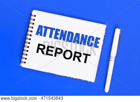 On A Blue Background, A White Ballpoint Pen And A White Notepad With The Text Attendance Report. Vie