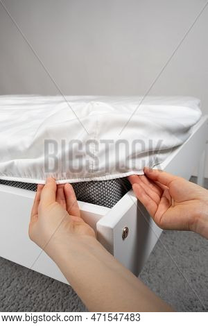A White Satin Sheet With An Elastic Band Is Put On The Mattress Of The Bed, A Close-up Of The Hands.