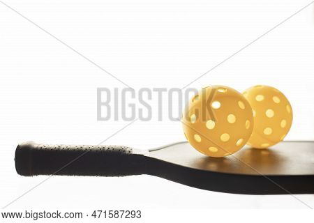 Closeup View Of Two Yellow Pickleballls On Top Of The Black Pickleball Racket With Glowing White Bac