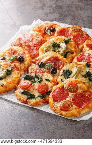Homemade Mini Pizzas Pizzette With Meaty And Vegetarian Toppings Close-up On Parchment On The Table.