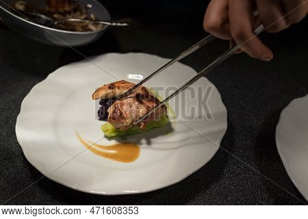 Chief Cook Putting Grilled Meat Piece Using Tweezers On Green Vegetables Puree White Plate With Sauc