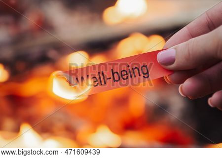 Small Red Sheet Of Paper With Word Well-being On It In Flames, Close Up. Concept Of Welfare, Wealth,