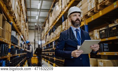 Manager In Suit Controlling Goods In A Waehouse.