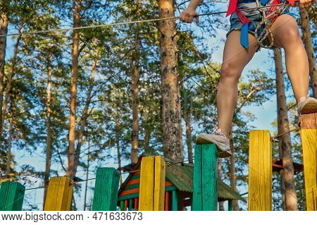 Bending Her Knees, The Girl In Pink Sneakers Slowly And Carefully Walks Along The Bars Of The Rope P