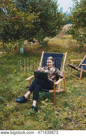 Beautiful Woman In Checkered Shirt With Laptop Working Outdoors In Garden, Home Office Concept. Remo