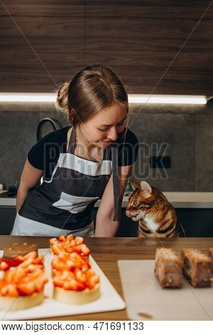 The Cat In The Apron Is Eating Dough In The Kitchen. Close-up