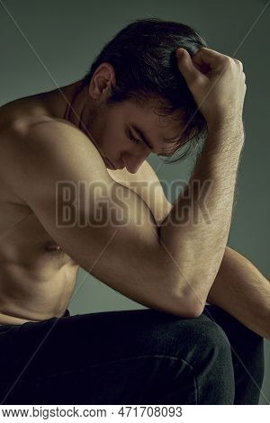 Thoughtful Young Man With Muscular Relief Body, Strong Hands Shape Sitting, Posing Shirtless In Blac