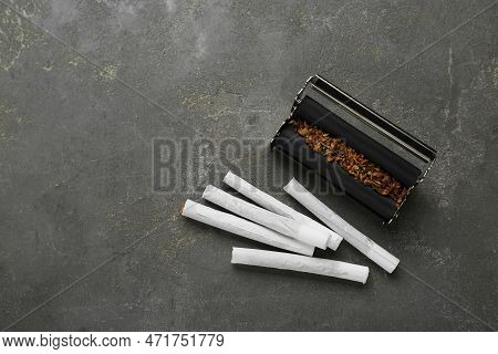 Roller With Tobacco And Hand Rolled Cigarettes On Dark Grey Table, Flat Lay. Space For Text