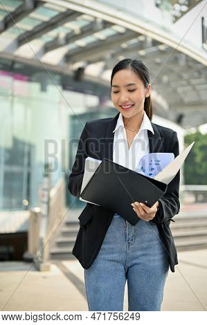 Busy Asian Female Ceo Checks A Financial Report In A Document File Outside Of The Company Building.