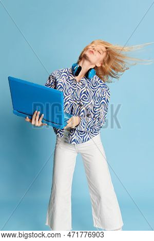 Happy Active Smiling Young Girl Listening To Music On Laptop And Dancing Over Blue Studio Background