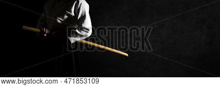 A Person In Black Hakama Standing In Fighting Pose With Wooden Sword Bokken Over Grungy Dark Backgro