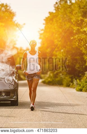 Young Sad Woman Standing Near The Road By The Broken Car In The Middle Of Nowhere. Smoke Coming Out