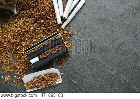 Flat Lay Composition With Roller And Tobacco On Dark Grey Table, Space For Text. Making Hand Rolled 