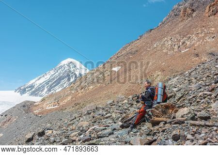 Tourist With Camera Sitting On Stone In High Mountains In Sunny Day. Scenic Alpine Landscape With Ma