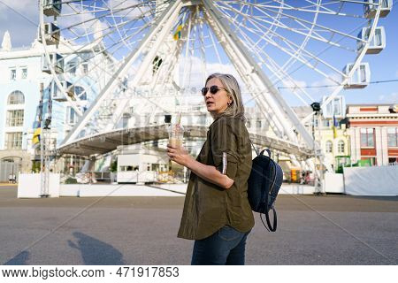Stylish And Confident Mature Woman With Grey Hair Enjoys Refreshing Juice Cup In Vibrant European Ci