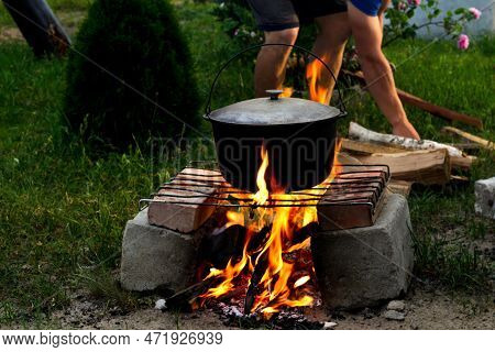 Defocus Man Cooking Fish Soup In The Iron Bowler Over A Campfire. Fish Soup Boils In Cauldron At The