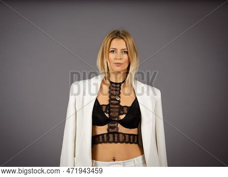 Portrait Of Blonde Woman With White Trousers Or Suit And Black Bralette, Underwear. Isolated On Gray