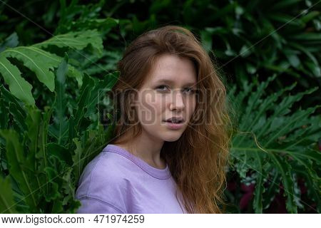 Portrait Of Young Woman Standing On An Ivy, Fern Wall Or In Greenery, Breathing, Smiling And Looking