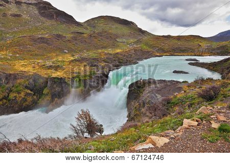 Affluent bustling Salto Grande waterfall with emerald water. On the edge of the cliff stands woman- tourist. Gorgeous National Park in Chilean Patagonia