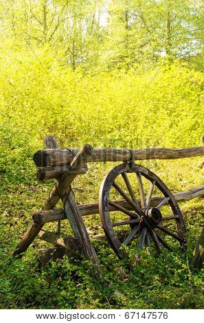 Old wagon wheel next to a wooden fence in the countryside.