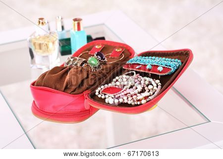 Handbag with accessorises and perfumes in bottles on table on  home interior background
