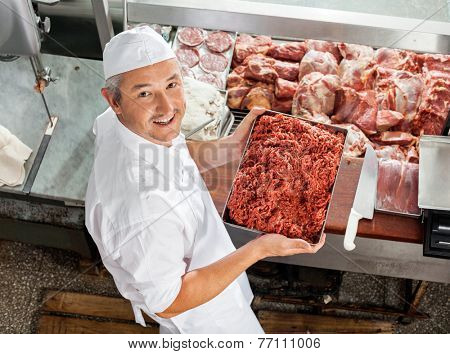High angle portrait of confident butcher holding minced meat at display cabinet in butchery