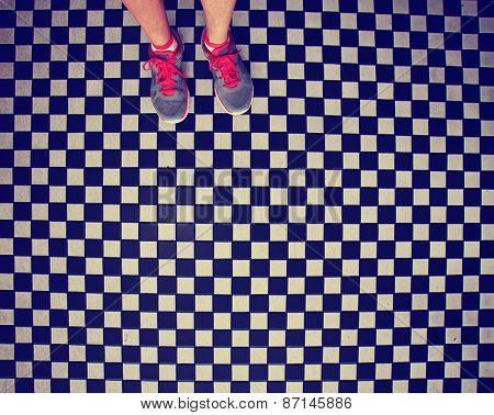 an overhead photo of a pair of tennis shoes on a grungy dirty checkered tile floor toned with a retro vintage instagram filter app or action