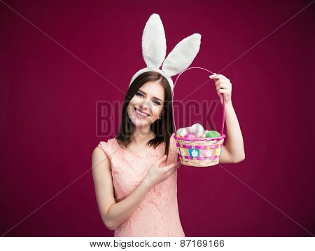 Happy young woman with an Easter egg basket over pink background. Looking at camera
