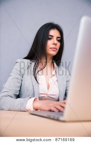 Young woman sittting at the table  and using laptop over gray background