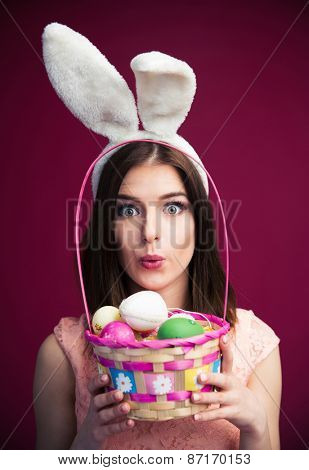 Cute young woman with an Easter egg basket over pink background. Looking at camera. 