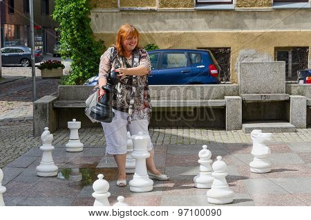 Young Cheerful Woman Holds Big Chess Piece On Street In Old Town Of Klaipeda