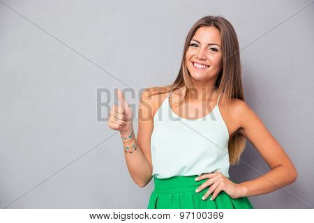 Portrait of a casual pretty woman showing thumb up over gray background and looking at camera