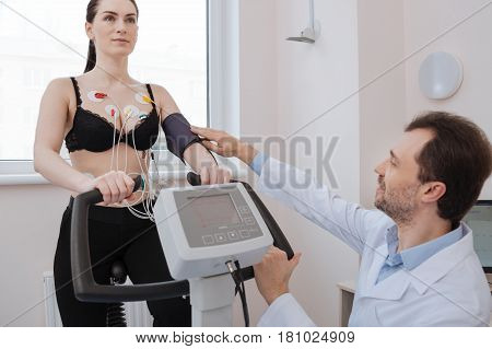 Just make it a little tighter. Lovely incredible competent cardiologist fixing the tonometer while a woman performing some exercises for indicating any possible heart pathologies