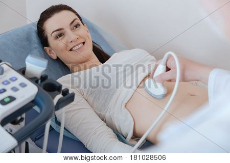 I feel happy. Enthusiastic emotional young lady paying a visit to the hospital and listening attentively to the experts words while experiencing sonography