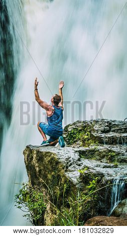 Man sitting in Front of Tegenungan Waterfall near Ubud raising hands and rhapsodize it, Bali, Indonesia.
