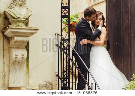 Groom Holds Bide's Face Tender Standing With Her On The Stairs Outside