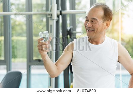Asian senior man holding glass of water at a gym. Tired thirstily. freshness.
