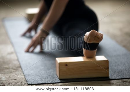 Young yogi woman practicing yoga concept, doing advanced splits, Straight Angle exercise, Samakonasana pose using blocks for deep stretch, working out on mat wearing black pants, leg close up, studio