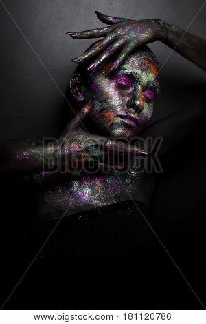 Young artistic woman in black paint and colourful powder. Glowing dark makeup. Creative body art on the theme of space and stars. Bodypainting project: art, beauty, fashion