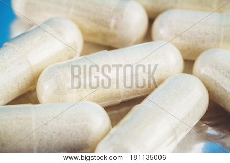 White capsules of glucosamine chondroitin healthy supplement pills on blue glossy background macro image