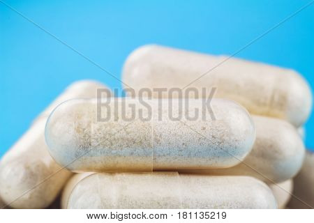 White capsules of glucosamine chondroitin healthy supplement pills in the spoon on blue background macro image