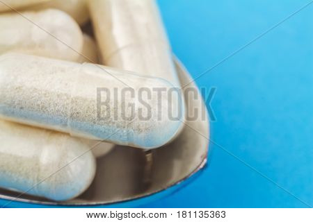White capsules of glucosamine chondroitin healthy supplement pills in the spoon on blue background macro image