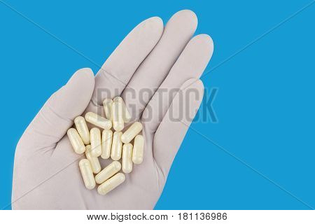 Hand in medical glove keeps lot of white capsules of glucosamine chondroitin healthy supplements pills blue background