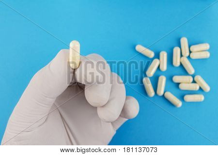 Hand in medical glove keeps one white capsule of glucosamine chondroitin healthy supplement pill on blue background macro image