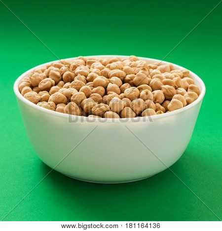 Raw chickpea or garbanzo bean in a bowl on green background. Vegan source of protein.