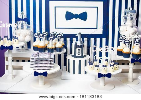 Cake, candies, marshmallows, cakepops, chocolate and other sweets on dessert table at kids birthday party. Birthday Dessert celebration candy bar in white and blue colors.