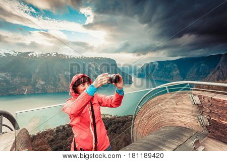 Tourism and travel. Woman tourist nature photographer taking photo with camera enjoying Aurland fjord landscape from Stegastein lookout Norway Scandinavia.