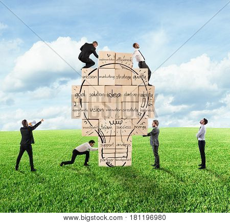 Business person built together a big brick wall with drawn lightbulb with business terms. Concept of creating a new idea.