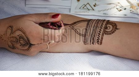On a white fabric there are two female hands. The hand of the master puts on a hand of model drawing henna.